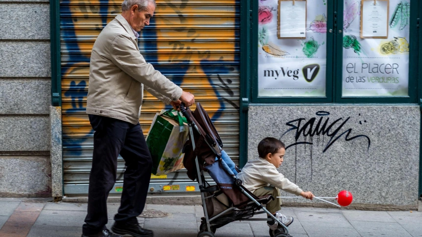 Un jubilado lleva una bolsa de plástico y un cochecito de bebé con un niño que tiene un globo rojo