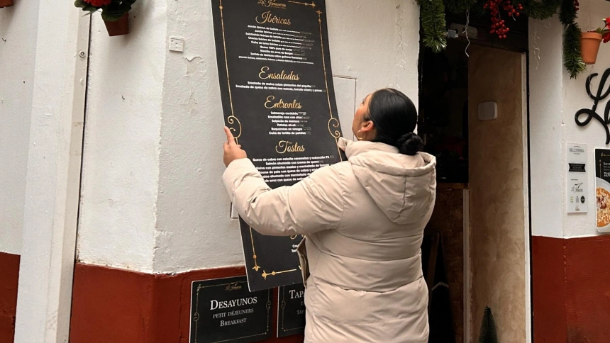 Una empleada instala los paneles informativos en la fachada de un establecimiento en la Judería.
