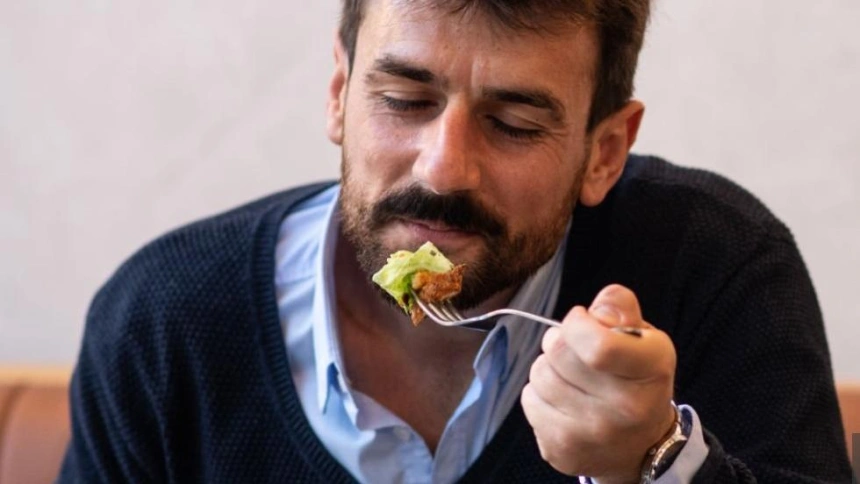 Attractive young businessman eating in a restaurant, while working on his laptop. Young entrepreneur on a business trip, working from his hotel restaurant. Handsome young businessman using modern technology for work.