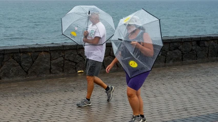 Dos personas pasean bajo la lluvia por el litoral de Arrecife