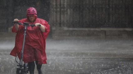 Una mujer circula con su patinete durante las lluvias