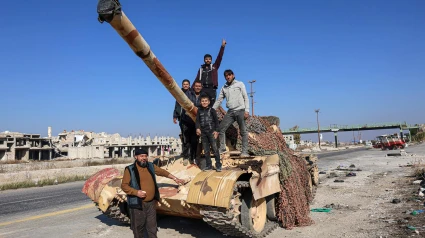 Un grupo de sirios se encuentran en la parte trasera de un tanque en la Autopista Internacional Alepo-Damasco M5, capturada por la oposición