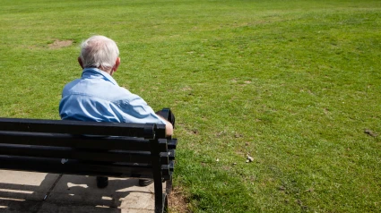 Un hombre anciano en un banco mirando hacia el parque