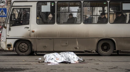 Los pasajeros de un autobús observan el cuerpo de una mujer tendido en la calle cubierto con una manta tras un bombardeo en el centro de Donetsk, Ucrania controlada por Rusia, el 20 de febrero de 2024