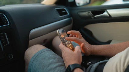 Primer plano de un hombre sentado en el asiento del pasajero de un automóvil, usando un teléfono inteligente mientras descansa en su regazo.