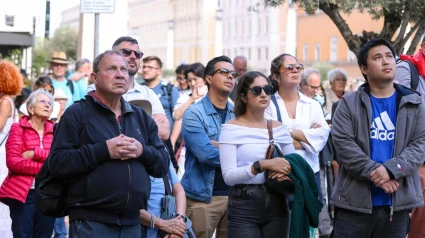 Los fieles observan una pantalla gigante que muestra imágenes de los cardenales electores mientras comienza el cónclave para elegir a un nuevo papa, en una calle que conduce a la Plaza de San Pedro en Roma.