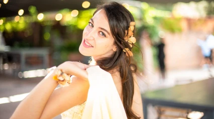 2HEWARR Young woman dressed in a yellow party dress smiling at camera. Wedding guest.