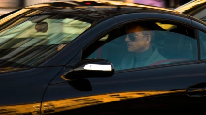 Hombre maduro con traje y gafas de sol conduciendo un coche negro en una calle de la ciudad