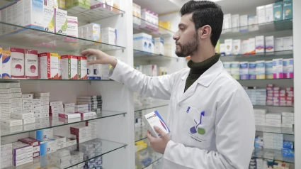 Un farmacéutico busca un medicamento en la estantería.