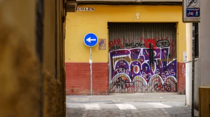 Un callejón estrecho, con una señal azul de giro a la izquierda y una puerta de garaje cubierta de grafitis, Sevilla, España.