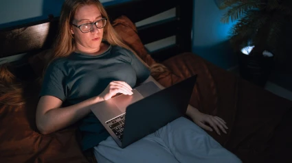 Mujer usando una computadora para ver una película sentada en la cama tarde en la noche en la oscuridad