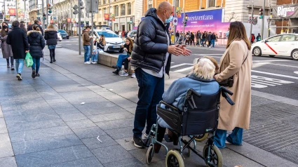 Hombre y mujer cuidando a una anciana en silla de ruedas en la calle de Madrid