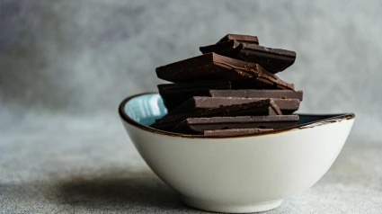 Montón de trozos de diferentes tipos de chocolate colocados en un recipiente de cerámica sobre una mesa gris borrosa