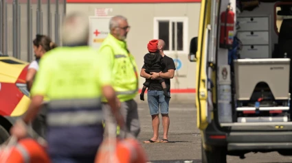 Un joven sujeta a un niño migrante en el puerto de La Restinga (El Hierro), tras el vuelco de un cayuco en el que han muerto siete personas