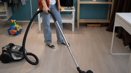 Una mujer limpia y aspira el suelo con una aspiradora en la sala de estar.