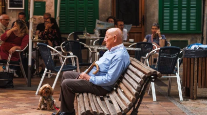 Un anciano con su perro descansa en un banco en un típico pueblo de montaña cerca de un café