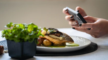 Una chica hace una foto a un plato de lubina marinada con setas y puré de patatas