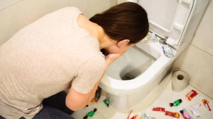 Young woman vomiting while binge eating of candies. A lot of candy wrappers on floo