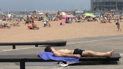 Un joven toma el sol en el paseo de la playa de Poniente, en Gijón
