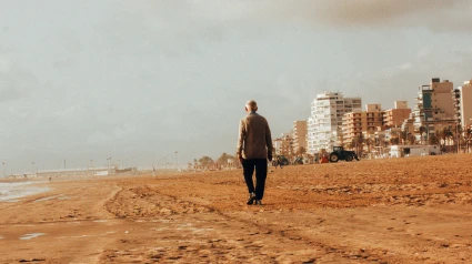 Un anciano solitario caminando por una playa de arena junto al océano por la mañana en Gandía