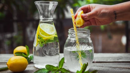 Un hombre exprime un limón sobre una jarra fresca de agua del grifo