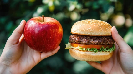 La mano derecha sujeta entre sus dedos una manzana y la derecha una hamburguesa