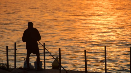 Silueta de un pescador contra el agua iluminada por el sol poniente, Salou, Costa Dorada