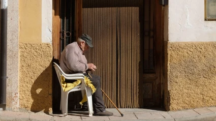 Un anciano con gorra de camionero se sienta al sol afuera de su casa en Libros, cerca de Teruel.