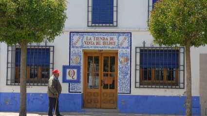 Un anciano con un bastón pasa junto a una tienda de recuerdos en Puerto Lápice, Ciudad Real.