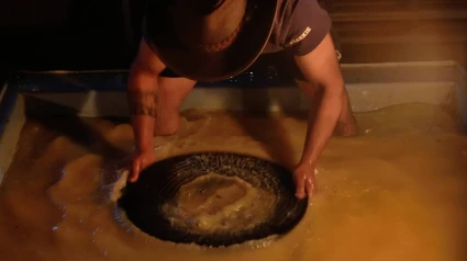 Una persona busca oro en una batea llena de agua