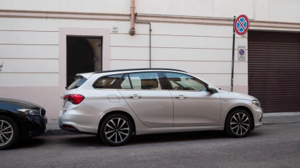 Moderno Fiat Tipo Station Wagon 1.6 Multijet 120 CV S Lounge plateado estacionado cerca de una señal de prohibido estacionar frente a un garaje.