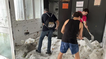 Operarios limpiando el granizo acumulado en el interior del edificio de los vestidores de la piscina municipal de la Seu d'Urgell.