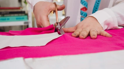 Primer plano de manos femeninas cortando tela con tijeras sobre una mesa en un taller de diseño de ropa de moda