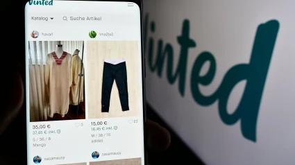 Persona sosteniendo un teléfono móvil con la página web de la empresa de mercado de segunda mano en línea Vinted delante del logotipo