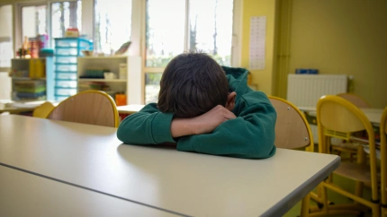 Un joven niño víctima del bullying pone su cabeza y sus brazos sobre la mesa
