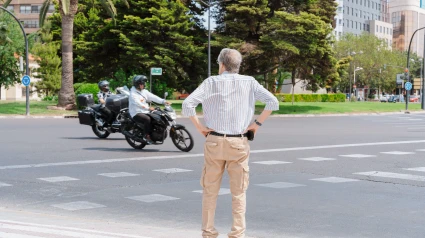 Un jubilado se encuentra en un cruce peatonal mientras dos motos pasan por una carretera de varios carriles en el centro de Valencia.