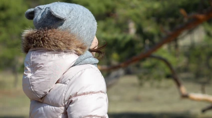 Una niña linda con un sombrero con orejas y una bufanda está de espaldas.