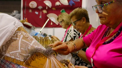 Dos mujeres realizan artesanía textil con bolillos en Feramur