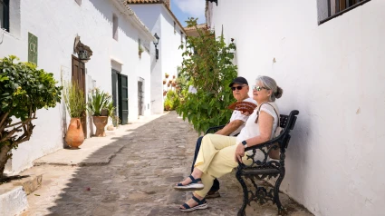 Una pareja de jubilados disfruta de un tranquilo paseo por un histórico pueblo blanco del sur de España, disfrutando del encanto y la tranquilidad de sus vacaciones.