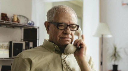 Una persona mayor con un teléfono en la mano atendiendo una llamada