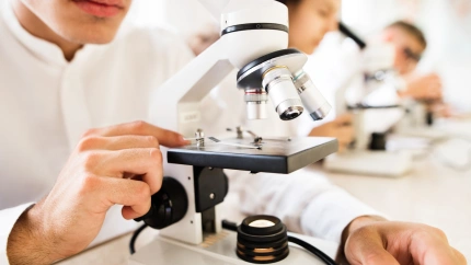 Unrecognizable high school students with microscopes in laboratory during biology class.