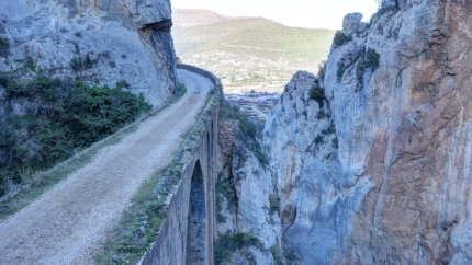 Un puente junto a un acantilado en Foz de Escalada, una brecha en las altas montañas rocosas del lago de La Pena, con árboles en las rocas, al atardecer, en Aragón, España.