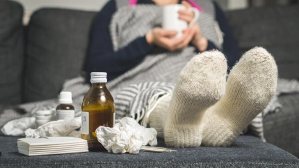 M45329 Cold medicine and sick woman drinking hot beverage to get well from flu, fever and virus. Dirty paper towels and tissues on table. Ill person.