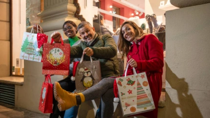 Happy friends showing Christmas shopping bags in front of a store at nigh