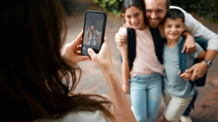 2JPBM71 2JPBM71 Mother taking a family photo on her phone of her happy little children and their father smiling before school. Boy and girl siblings with their dad
