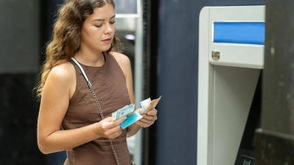 Una linda joven con vestido contando dinero después de retirarlo de la tarjeta en un cajero automático en una calle de la ciudad