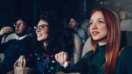 Group of young people sitting in modern cinema and watching funny movie. They are happy and laughing