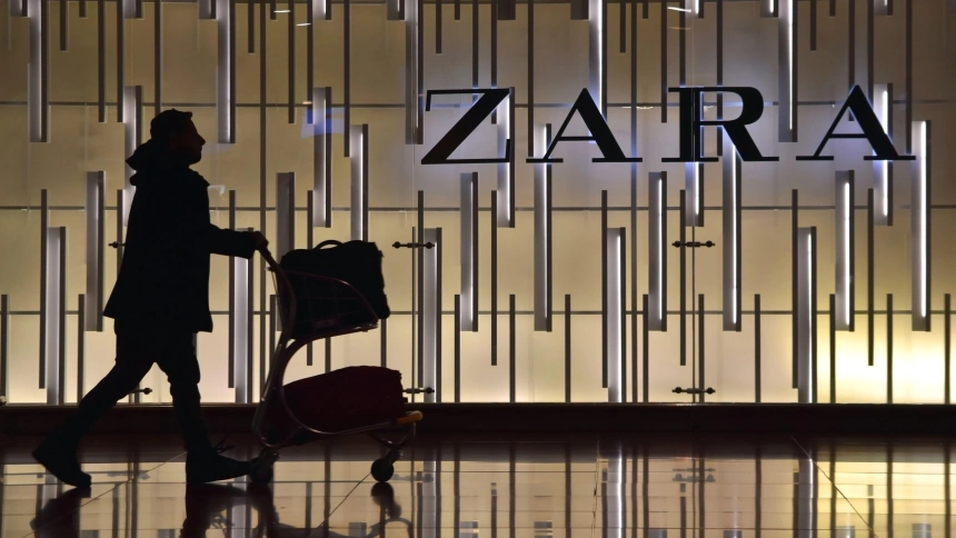 Silueta de una mujer empujando un carrito de equipaje frente al escaparate de una tienda Zara, en el aeropuerto de El Prat, Barcelona, España.