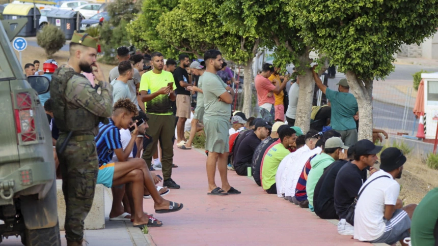 Varios migrantes observan desde lejos a los cientos de vecinos de Ceuta han trasladado este martes hasta la plaza de los Reyes, frente a la Delegación del Gobierno, la protesta contra el posible alojamiento de migrantes en distintos puntos de la ciudad