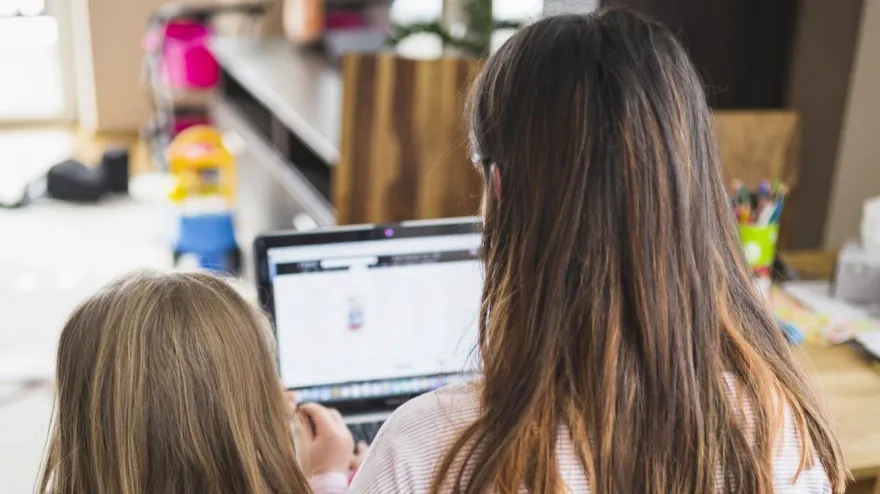 Una mujer trabajando en su ordenador mientras cuida de su hija